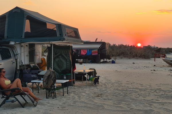 A women on a camp chair reclining in front of a tent at the beach with a sunset